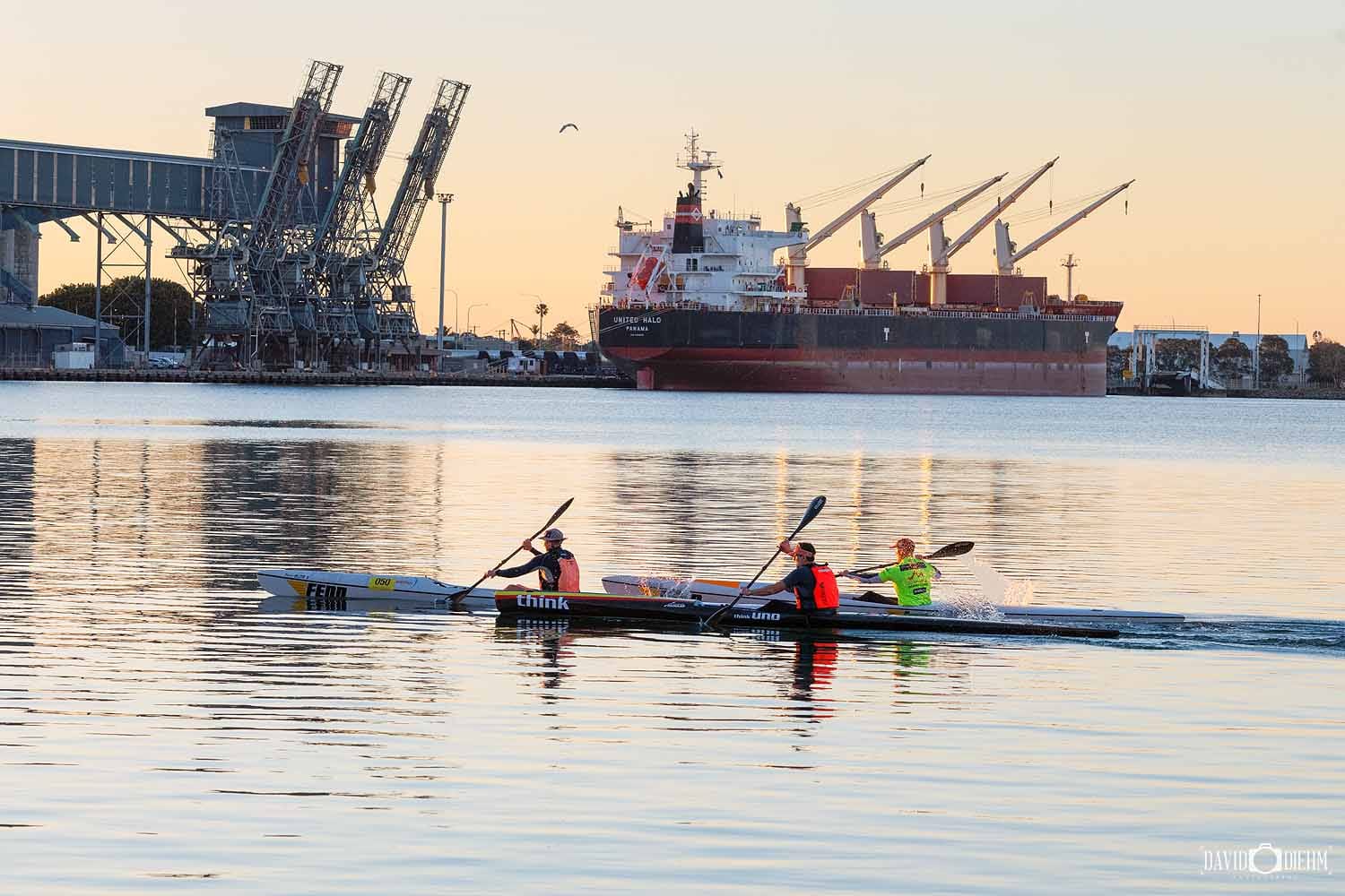 Kayakers paddling across Newcastle Harbour near Honeysuckle with a cargo ship in the background.