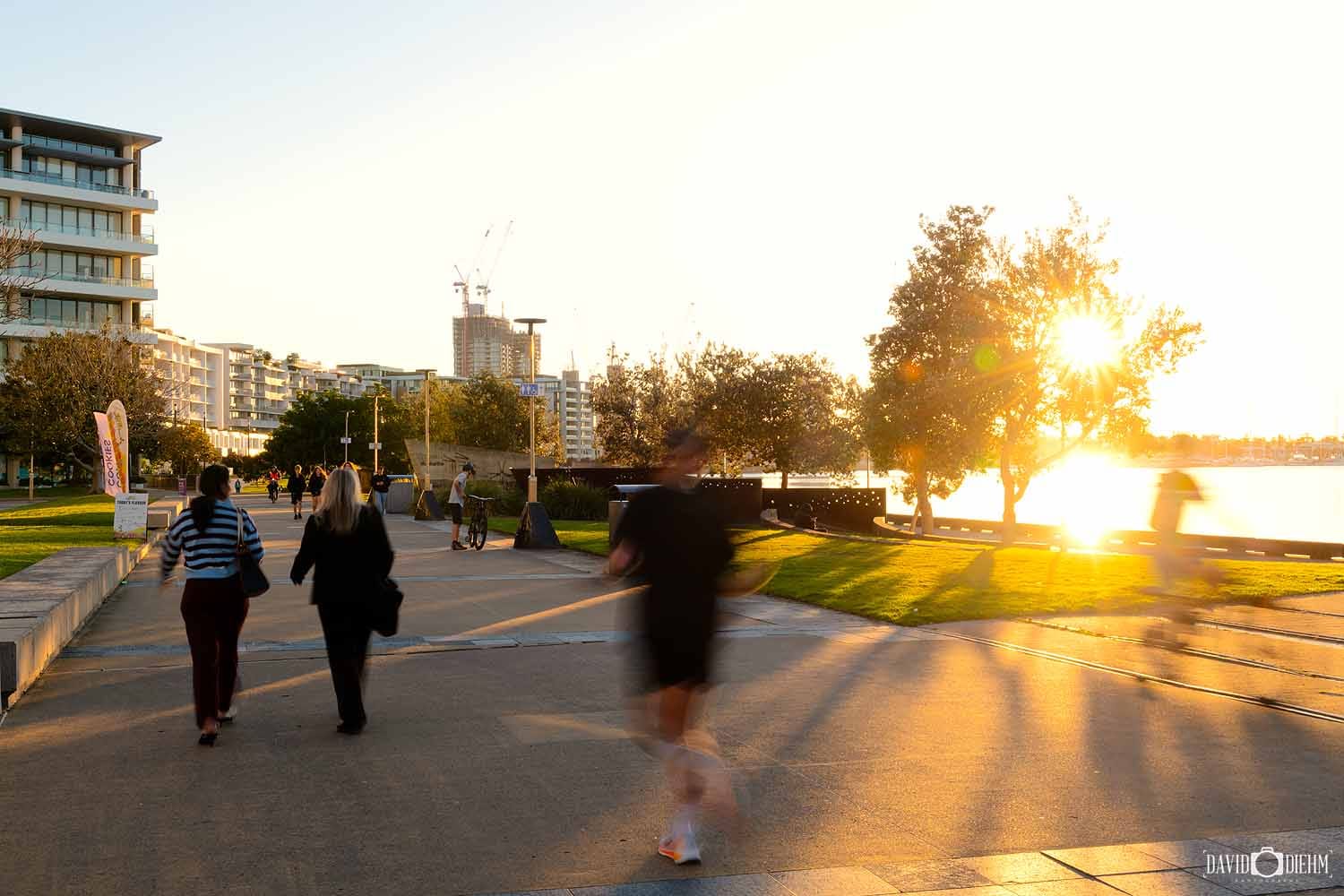 People walking along Honeysuckle Foreshore Walk at sunset beside Newcastle Harbour.