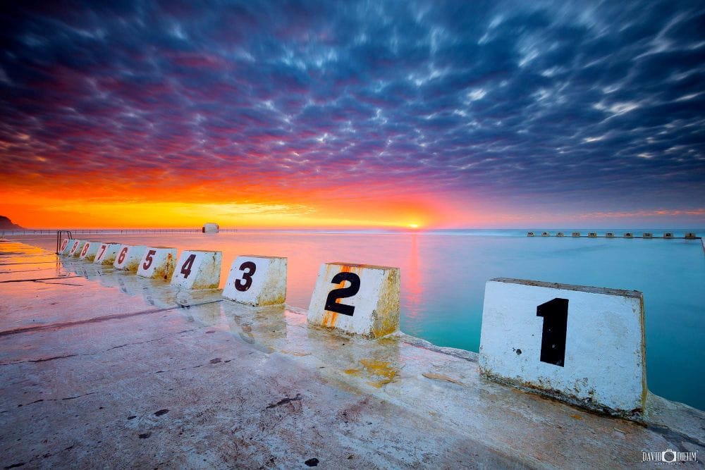 merewether-ocean-baths-sunrise-lap-markers.jpg Sunrise over Merewether Ocean Baths with the iconic numbered lap markers reflected in calm ocean water.