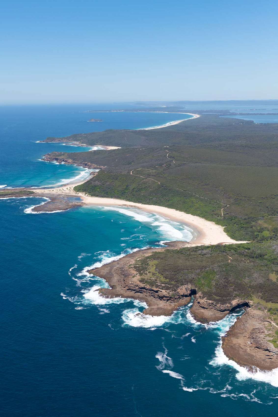 Aerial panorama of Moonee Beach and the rugged Munmorah coastline featuring pristine beaches, rocky headlands, native bushland and the Pacific Ocean near Lake Macquarie NSW.