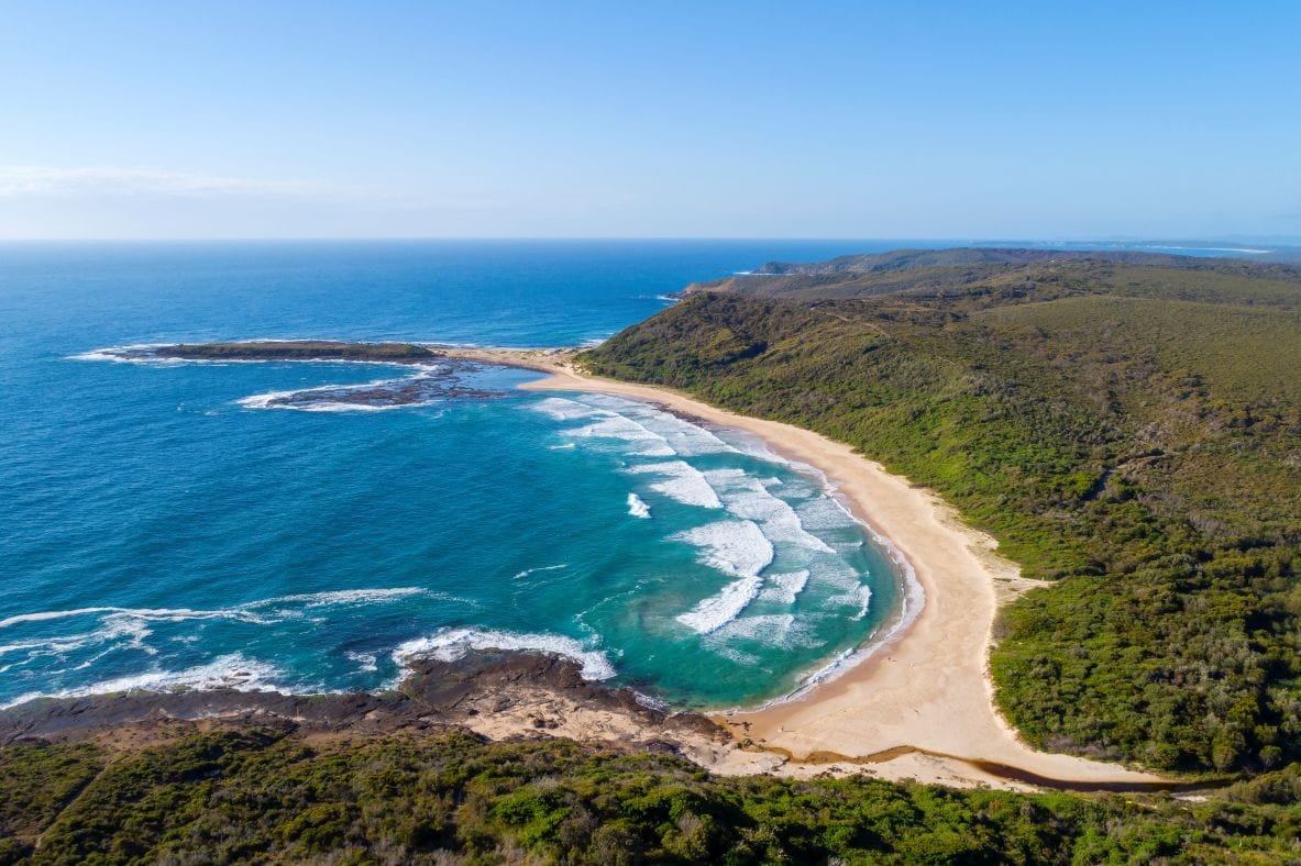 Aerial view of Moonee Beach in Munmorah State Conservation Area showing turquoise water, sweeping sandy shoreline, rocky headlands and untouched coastal bushland near Lake Macquarie.