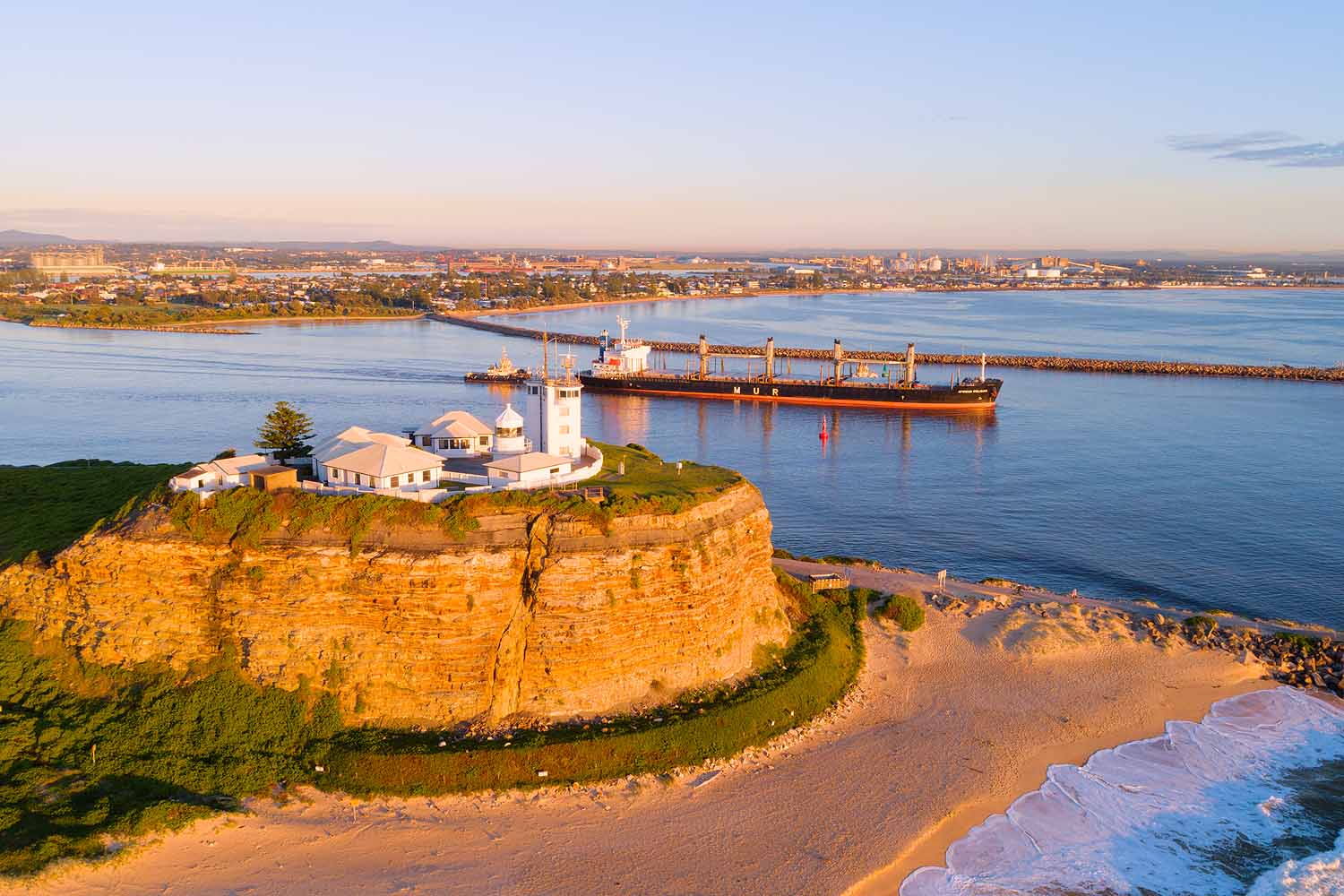 Aerial view of Nobbys Lighthouse overlooking Newcastle Harbour and a coal ship entering the harbour in Newcastle NSW.