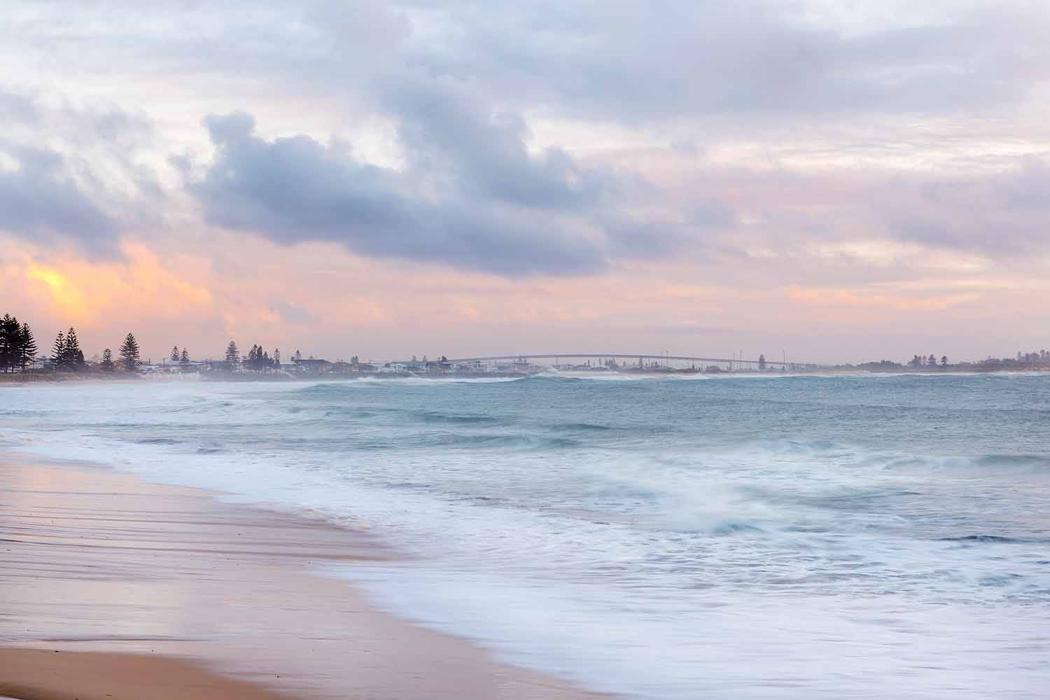 Sunrise over Stockton Beach in Newcastle NSW looking north towards Stockton Bridge with rolling waves and colourful morning skies.