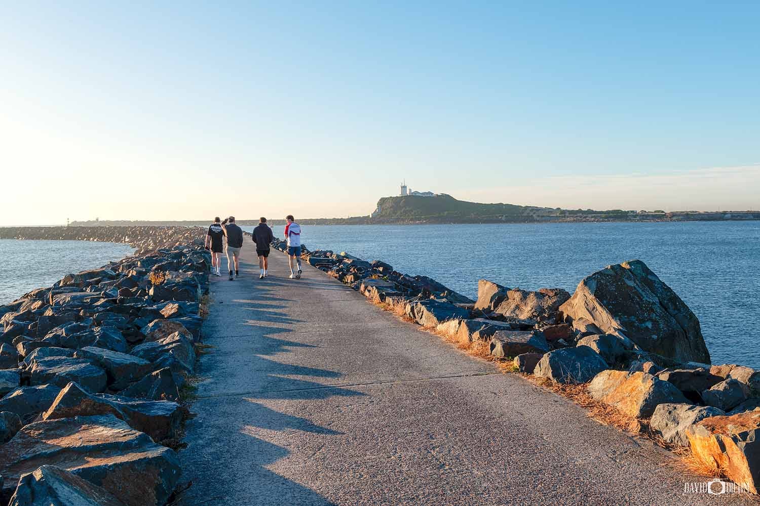 People walking along the Stockton Breakwall on the Shipwreck Walk overlooking Newcastle Harbour.