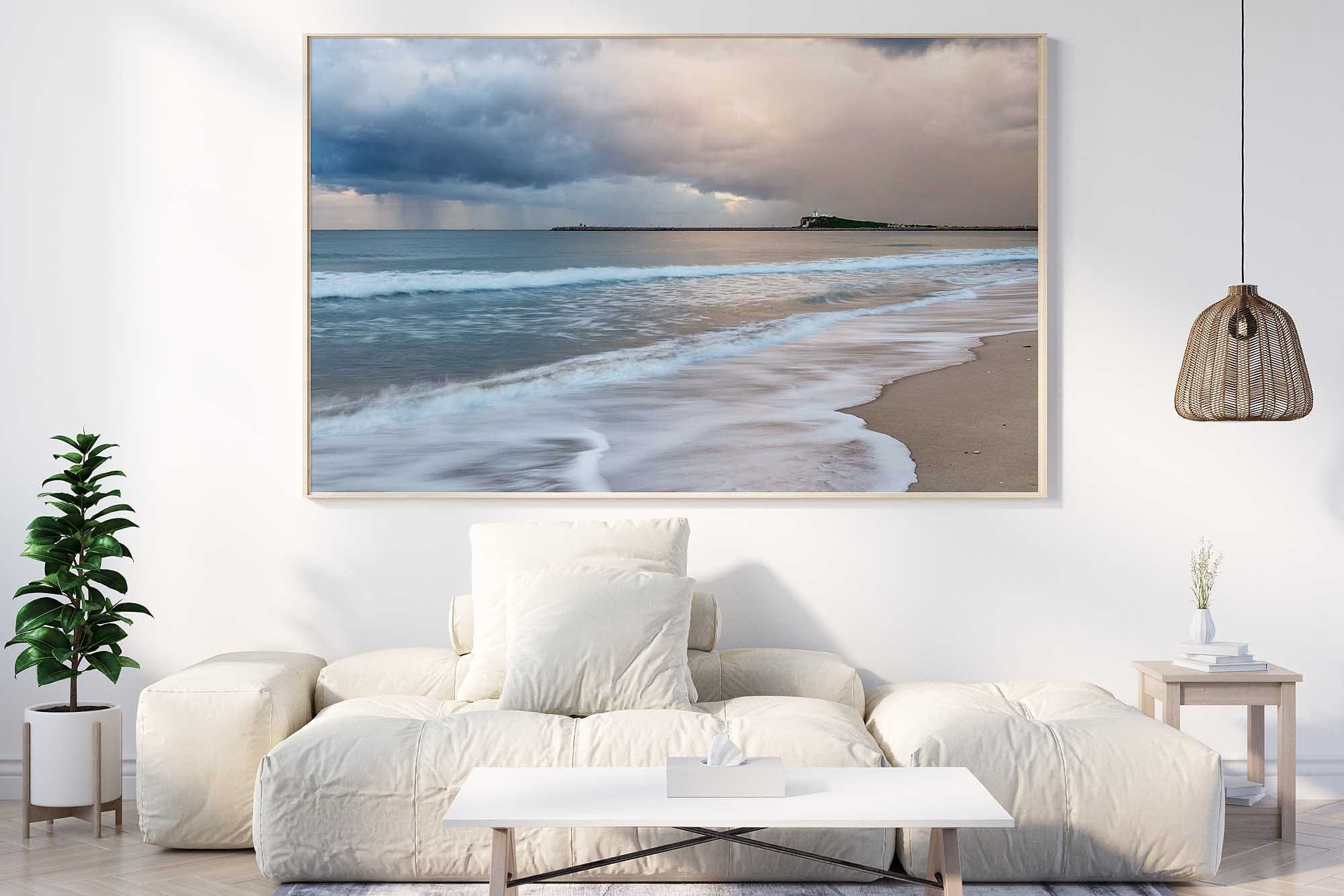 Framed coastal wall art featuring Stockton Beach and Nobbys Lighthouse beneath dramatic storm clouds displayed in a modern living room.