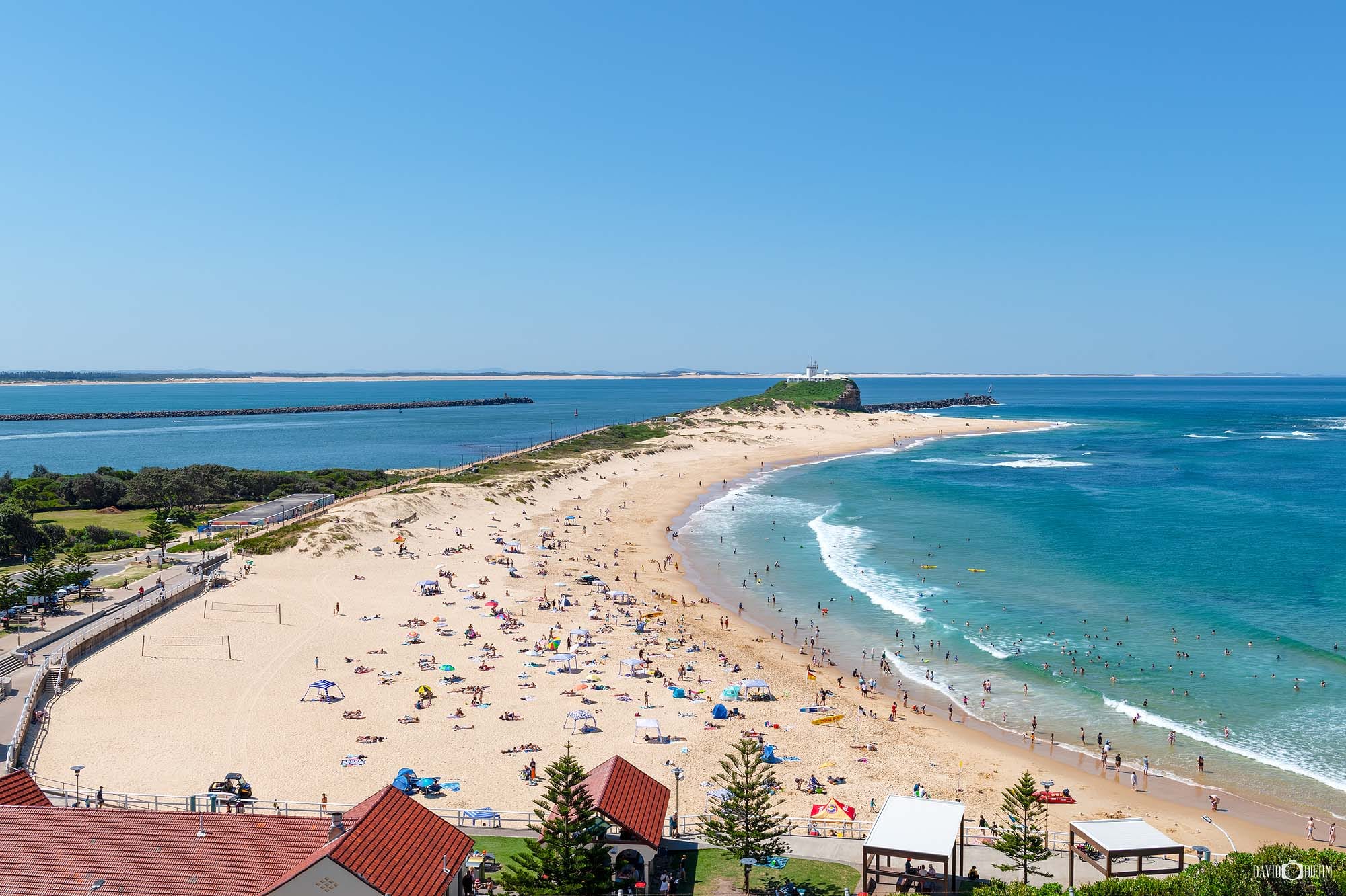 Aerial view of Nobbys Beach and Nobbys Headland on a busy summer day in Newcastle NSW.