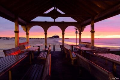 Sunrise viewed through Nobbys Pavilion overlooking Nobbys Beach and Nobbys Lighthouse in Newcastle NSW.