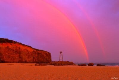 Rainbow over Redhead Beach in Lake Macquarie NSW, with the iconic shark tower beneath a dramatic pink and red sky.