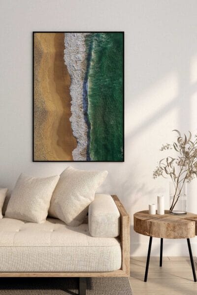 Coastal Rhythm aerial beach photography print displayed in a black frame above a neutral sofa in a contemporary living room.