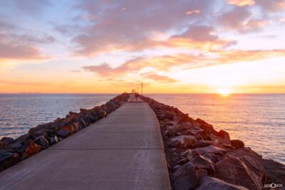 Spectacular sunrise over Stockton Breakwall in Newcastle NSW, with vibrant pink and golden clouds illuminating the ocean and rocky breakwater.