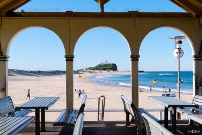 Afternoon view of Nobbys Beach and Nobbys Head in Newcastle NSW, framed by the arches of the Nobbys Beach pavilion.