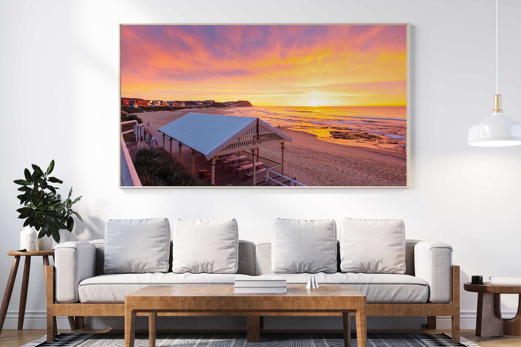 Framed landscape photograph of Merewether Beach Pavilion at sunrise, displayed above a lounge in a contemporary living room.