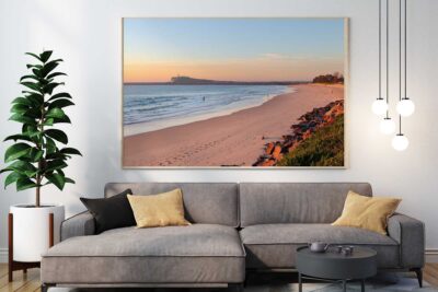 Stockton Beach Golden Glow coastal photography print displayed in a natural timber frame above a grey sofa in a contemporary living room.