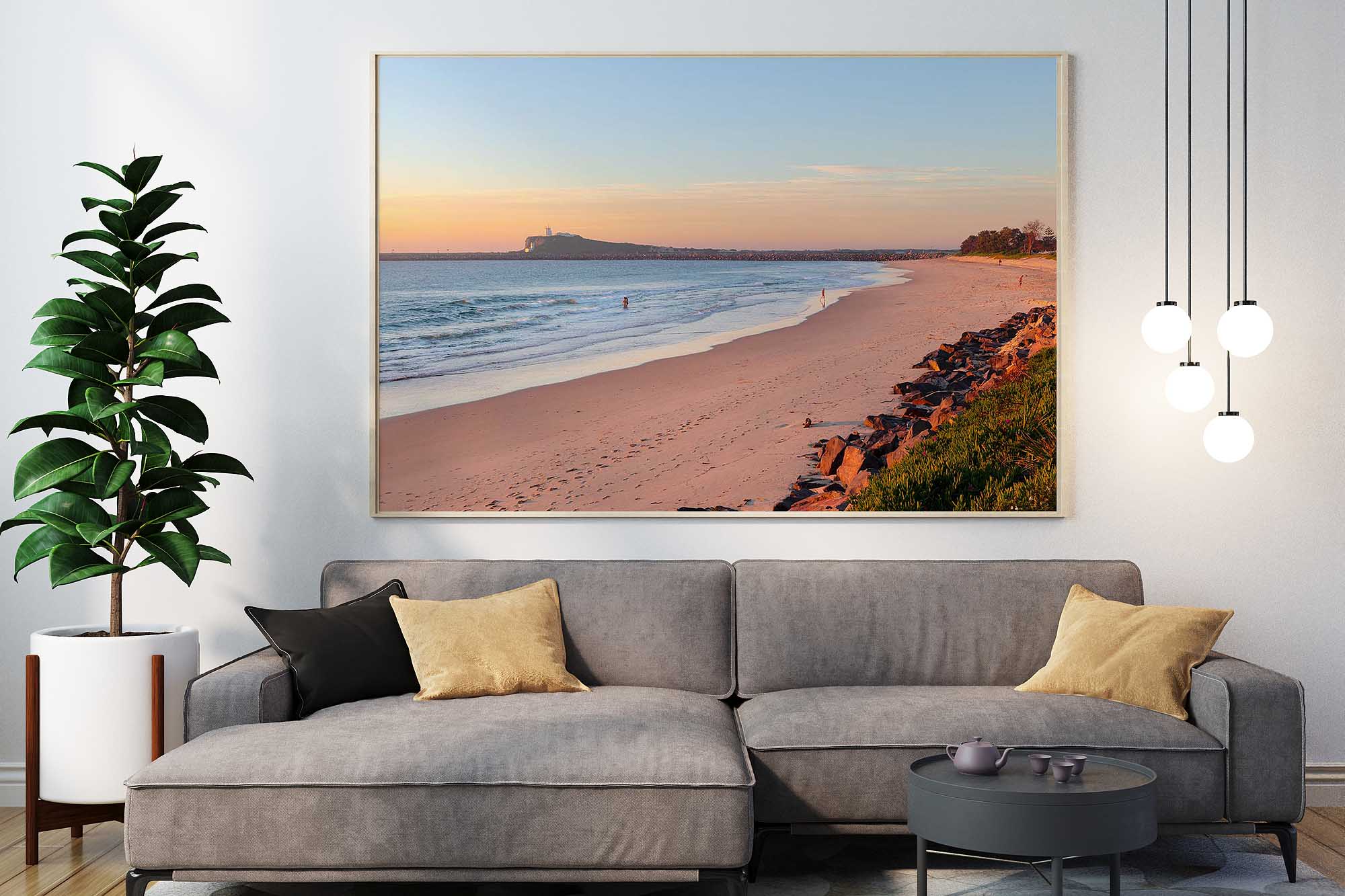 Stockton Beach Golden Glow coastal photography print displayed in a natural timber frame above a grey sofa in a contemporary living room.