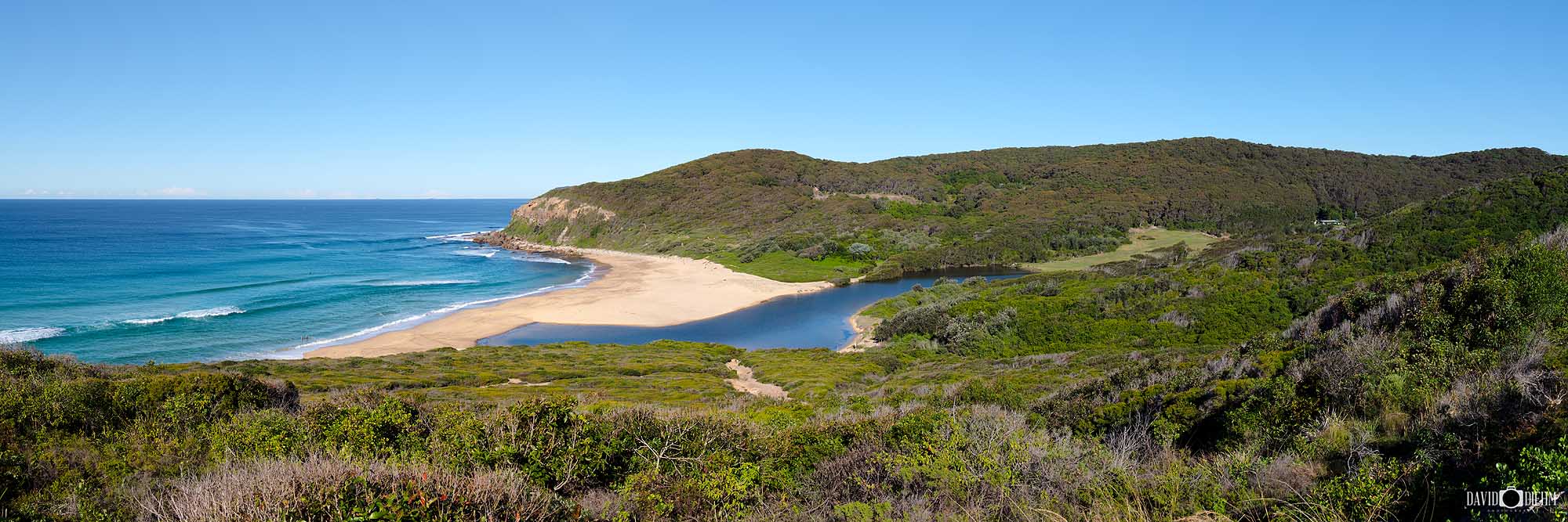 Panoramic landscape photograph of Glenrock State Conservation Area near Newcastle NSW, featuring Glenrock Lagoon, a secluded sandy beach, turquoise ocean and surrounding coastal bushland.